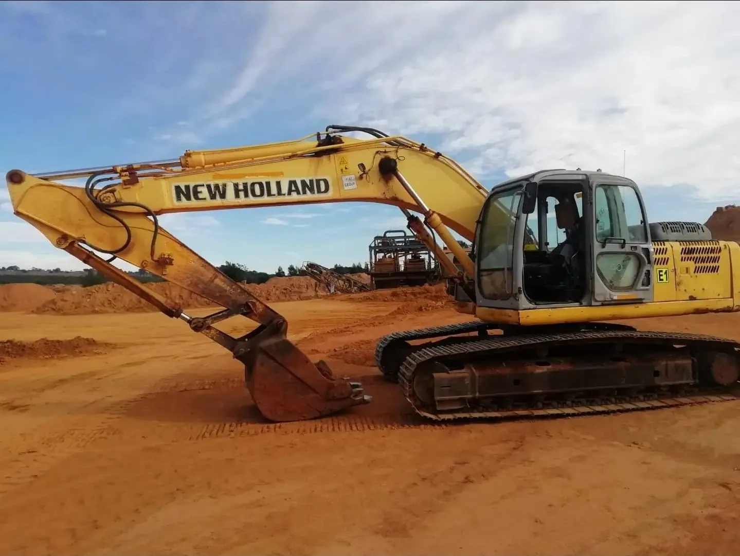 A yellow New Holland tracked excavator standing on a levelled borrow area.