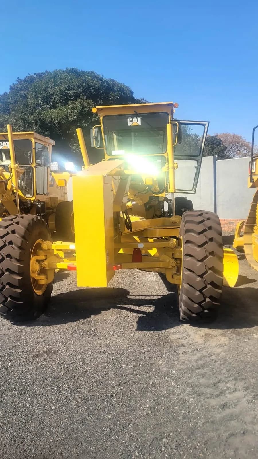 A yellow Caterpillar motor grader parked in the yard.
