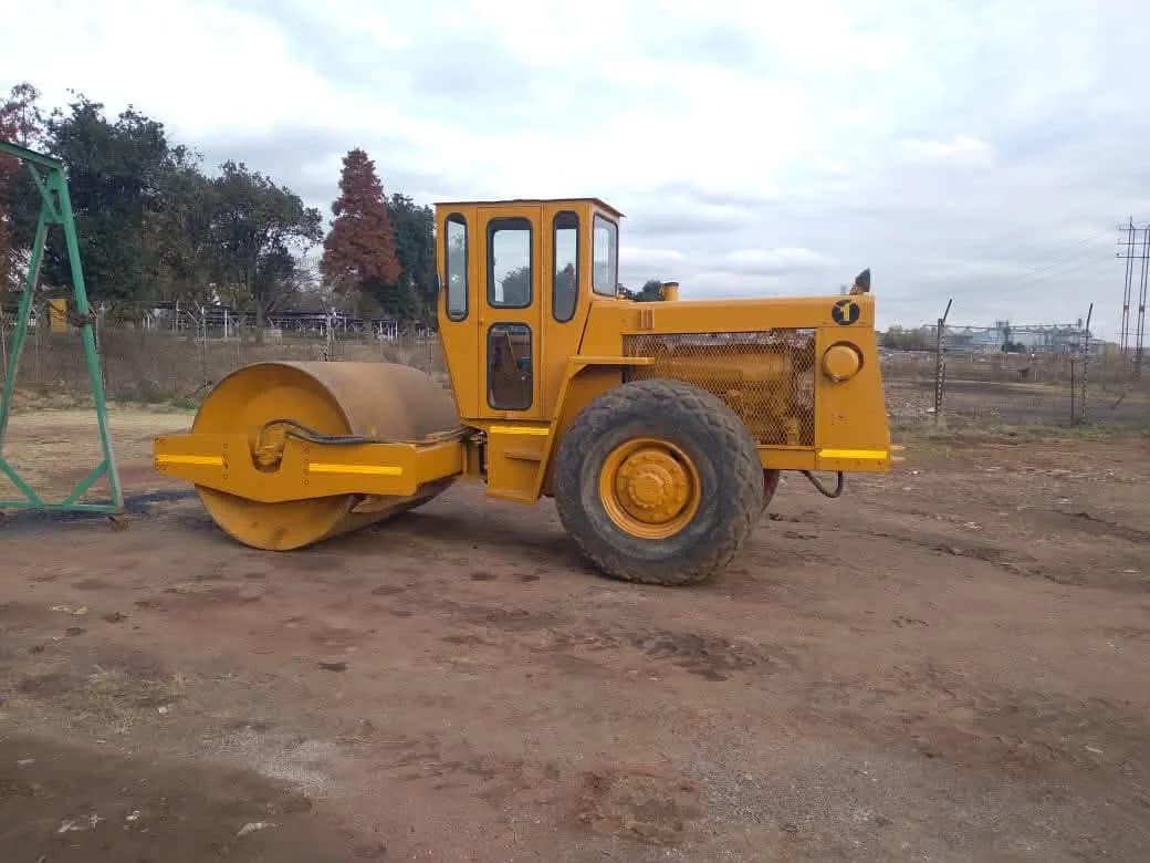 A yellow single-drum vibratory roller parked on open ground.
