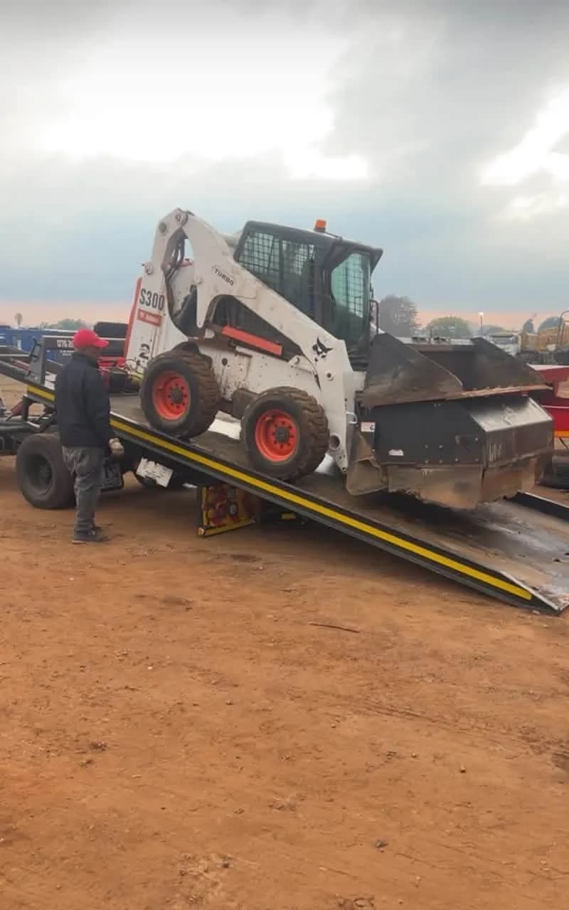 A white Bobcat S300 skid steer loader being loaded onto a trailer via ramps.