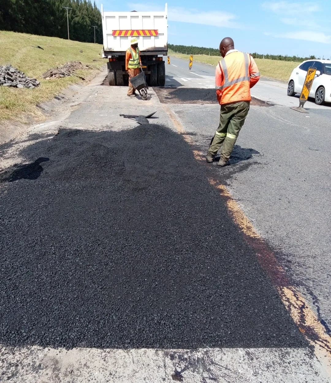 Fresh asphalt being spread by hand into a prepared road patch.