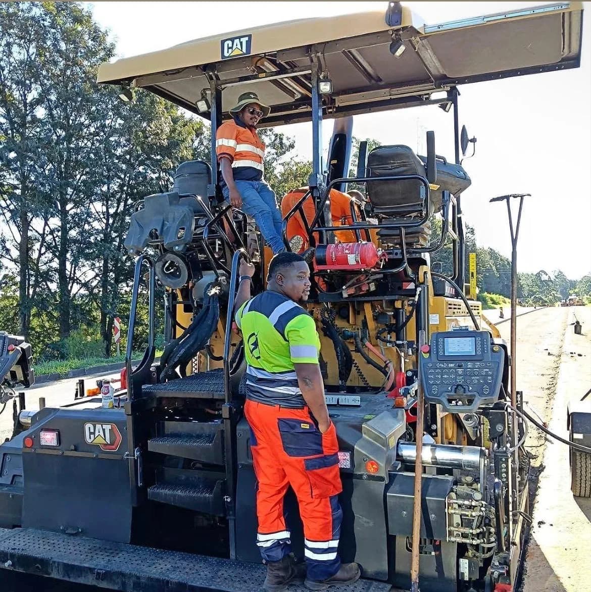 Two crew members working on a CAT paver laying a new surfacing layer.