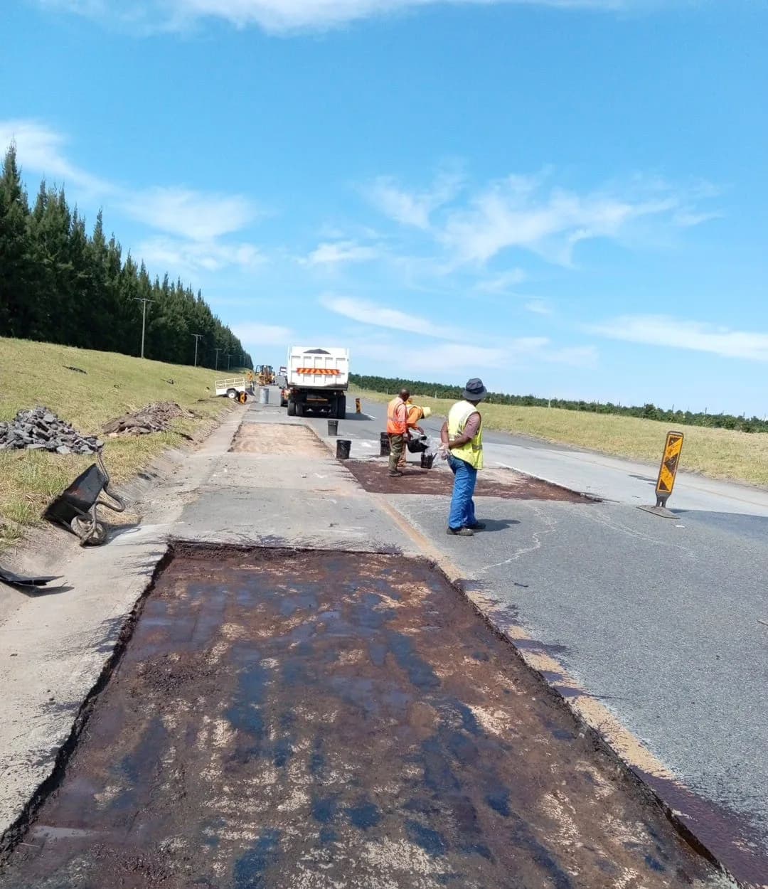A rectangular section of road surfacing cut out and coated with black tack coat.