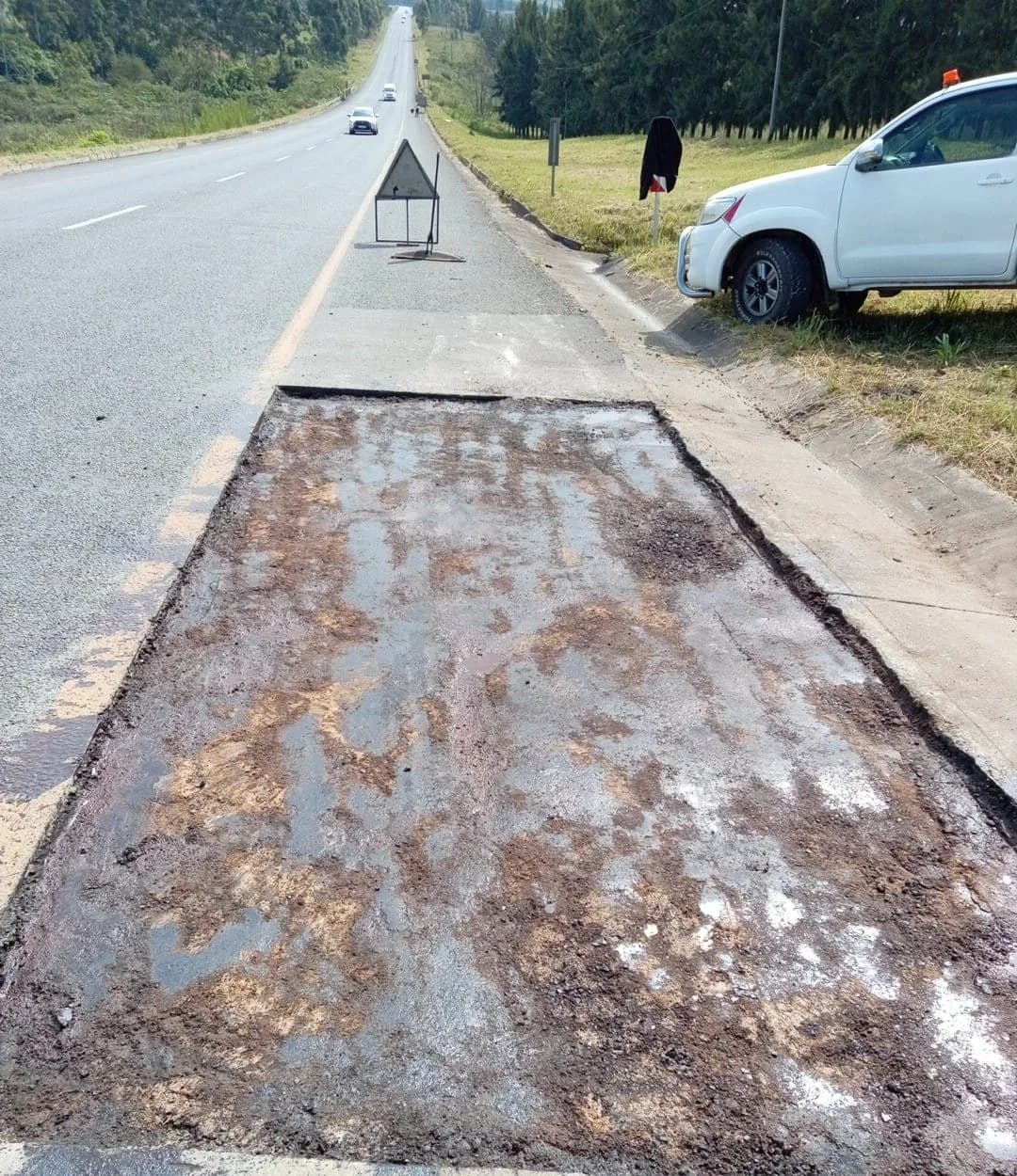 Prepared road patch with a warning triangle and chevron board set out beyond.
