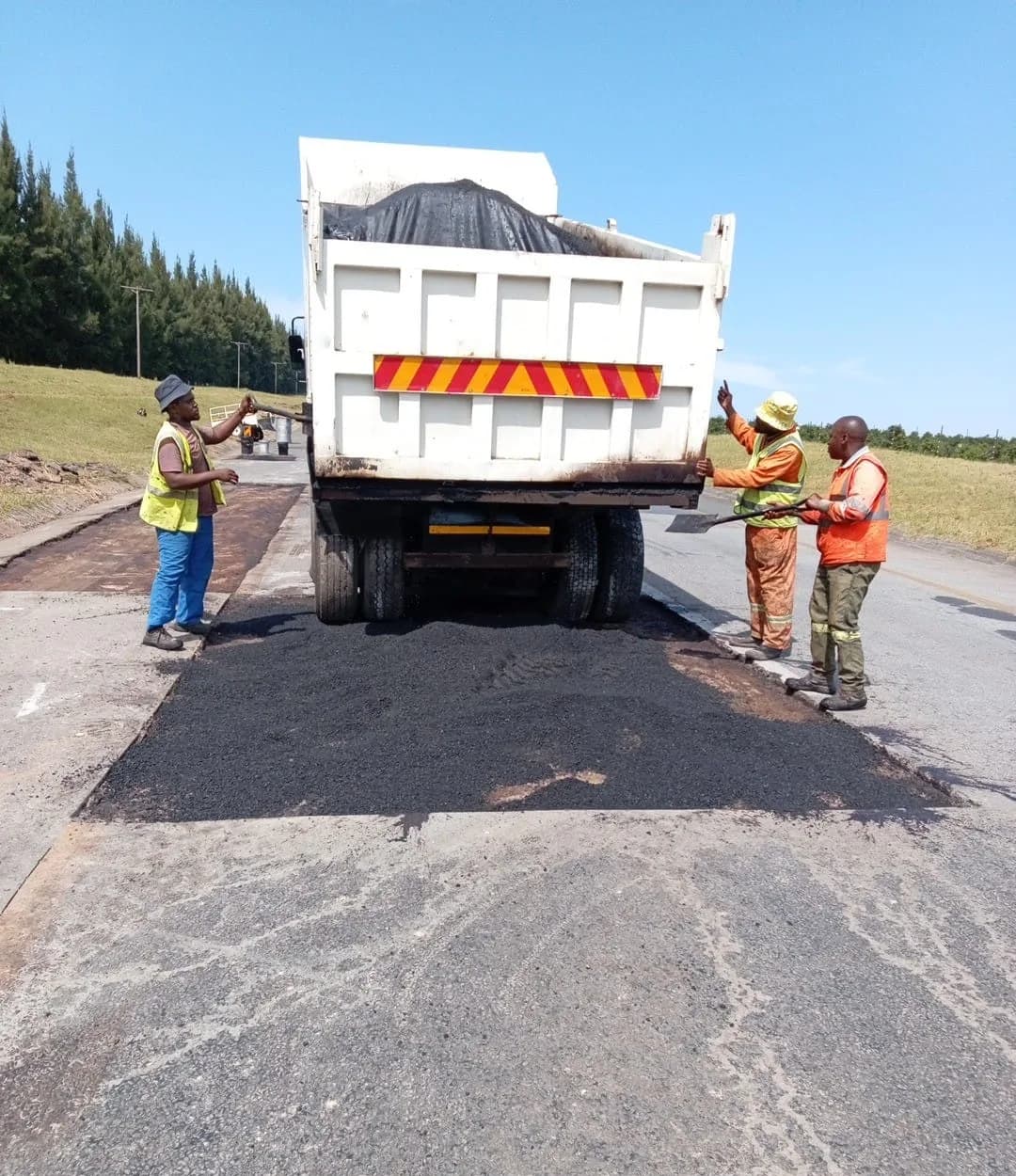 A tipper truck discharging asphalt with crew spreading it with shovels.
