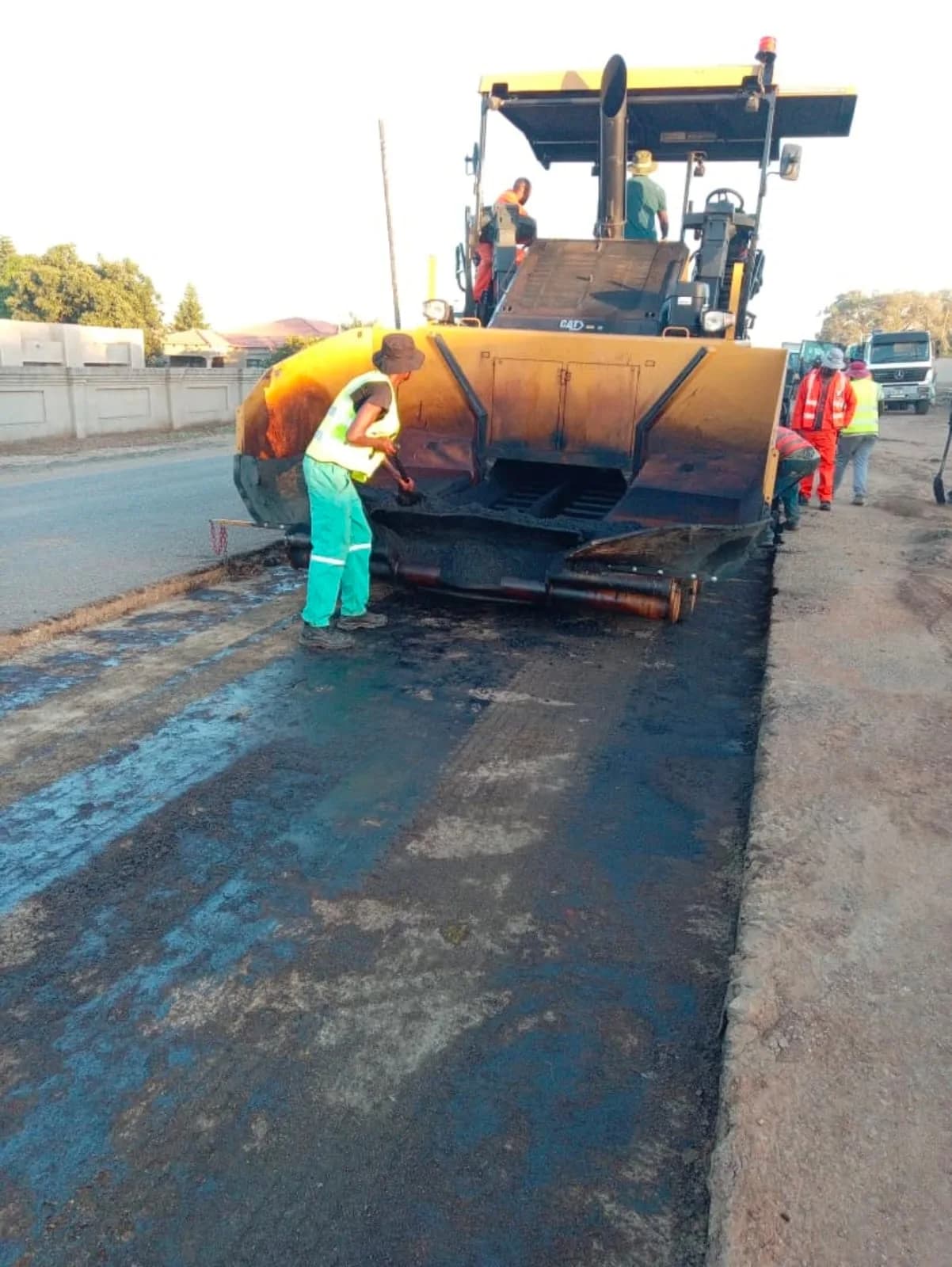 An Izanolihle Roads crew member working at the hopper of an asphalt paver, with the crew alongside.